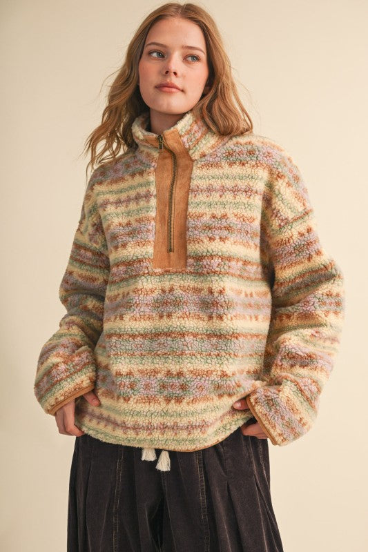 A woman wearing a fuzzy quarter-zip pullover sweater with horizontal multicolor stripes in beige, green, orange, and brown, paired with dark pants, against a plain beige background.